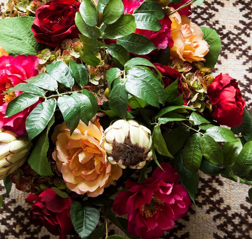 A bouquet of vibrant flowers featuring red and peach-colored roses, surrounded by lush green leaves, is placed on a patterned black and white surface.